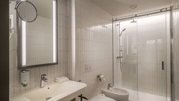 A modern bathroom with a large mirror, two sinks, a toilet, and a glass-enclosed shower.