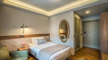 Una habitación de hotel con una cama, una mesita de noche con un florero, un sillón verde, un cabecero de madera, un espejo grande y un armario de madera.