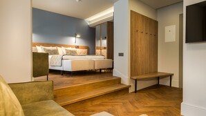 A modern bedroom with a large bed, a wooden wardrobe, and a seating area with a sofa and armchair. - Hotel Vilnia (Vilnius)