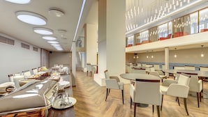 A modern dining area with multiple tables and chairs, a buffet setup, and a staircase leading to an upper level. - Hotel Vilnia (Vilnius)