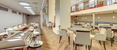 Un comedor moderno con varias mesas y sillas, una barra de buffet y una escalera que lleva a un nivel superior.