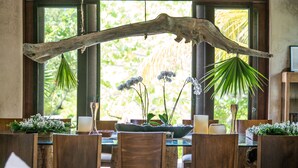 A dining area with wooden furniture, a large window with a view of greenery, and a rustic wooden beam above the table. - Casa Maya Kaan (Tulum)
