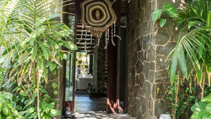 A stone pathway leading to a wooden door with a woven hanging ornament. - Casa Maya Kaan (Tulum)