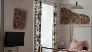 Un dormitorio con cama de madera, un escritorio con televisor, un espejo y una lámpara en el techo.
