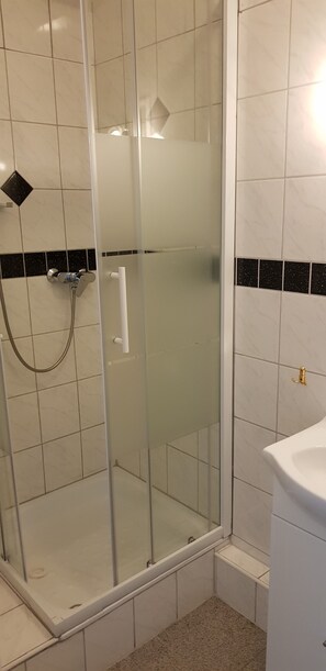 Une cabine de douche fermée par des parois en verre, avec un lavabo blanc et un mur recouvert de carreaux noirs.