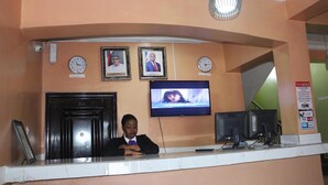 Un mostrador de recepción con un reloj, cuadros enmarcados, un televisor y una cámara de seguridad.