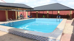 Una piscina con borde a cuadros, un área de estar cubierta y un edificio de fachada roja y tejado gris.