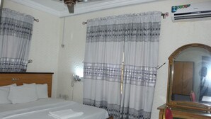 Una habitación de hotel con cama, cortinas, un espejo y un equipo de aire acondicionado.