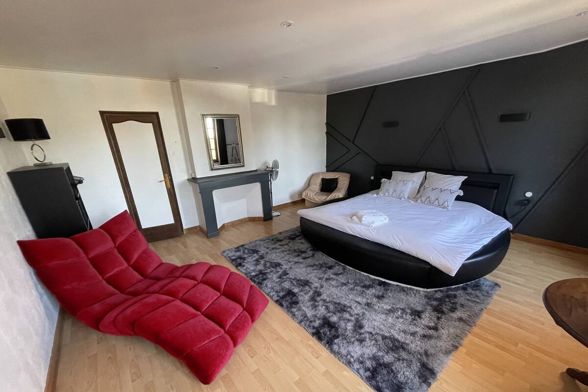 A modern bedroom with a large bed, a red chair, a desk, and a mirror.