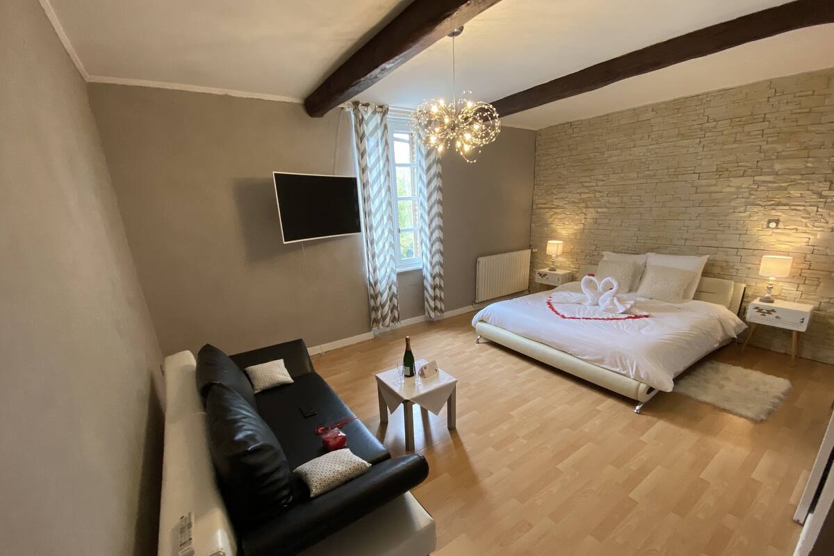 A modern bedroom with a large bed, a sofa, a TV, and a stone wall.