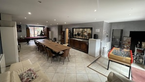 Un amplio salón con una mesa de comedor, sofás, mesa de billar y mesa de fútbolín.