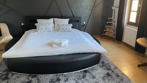 Un dormitorio moderno con una cama grande, cabecera, mesita de noche, lámpara, ventana y radiador.