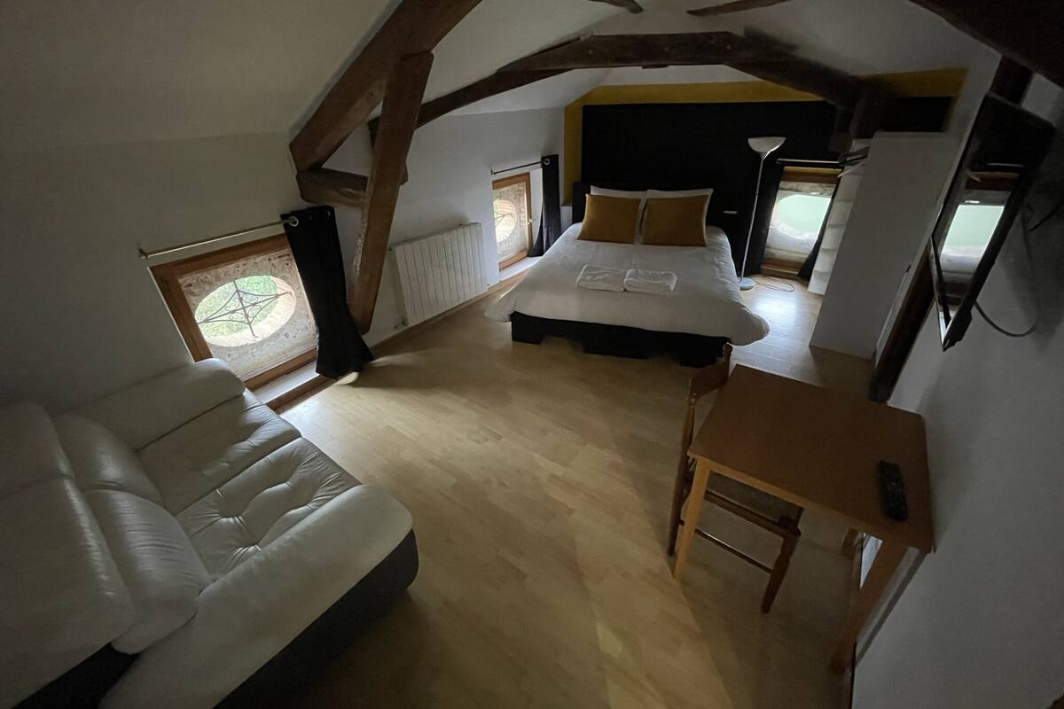 A bedroom with a large bed, a sofa, a small table, and a window with a view.