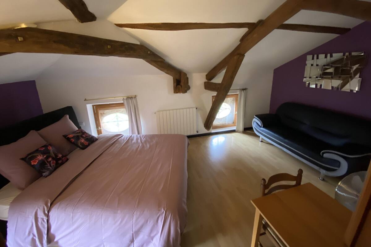 A bedroom with a bed, a sofa, a wooden table, and a window.