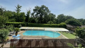 Una piscina con zona cubierta, rodeada de abundante vegetación y árboles.
