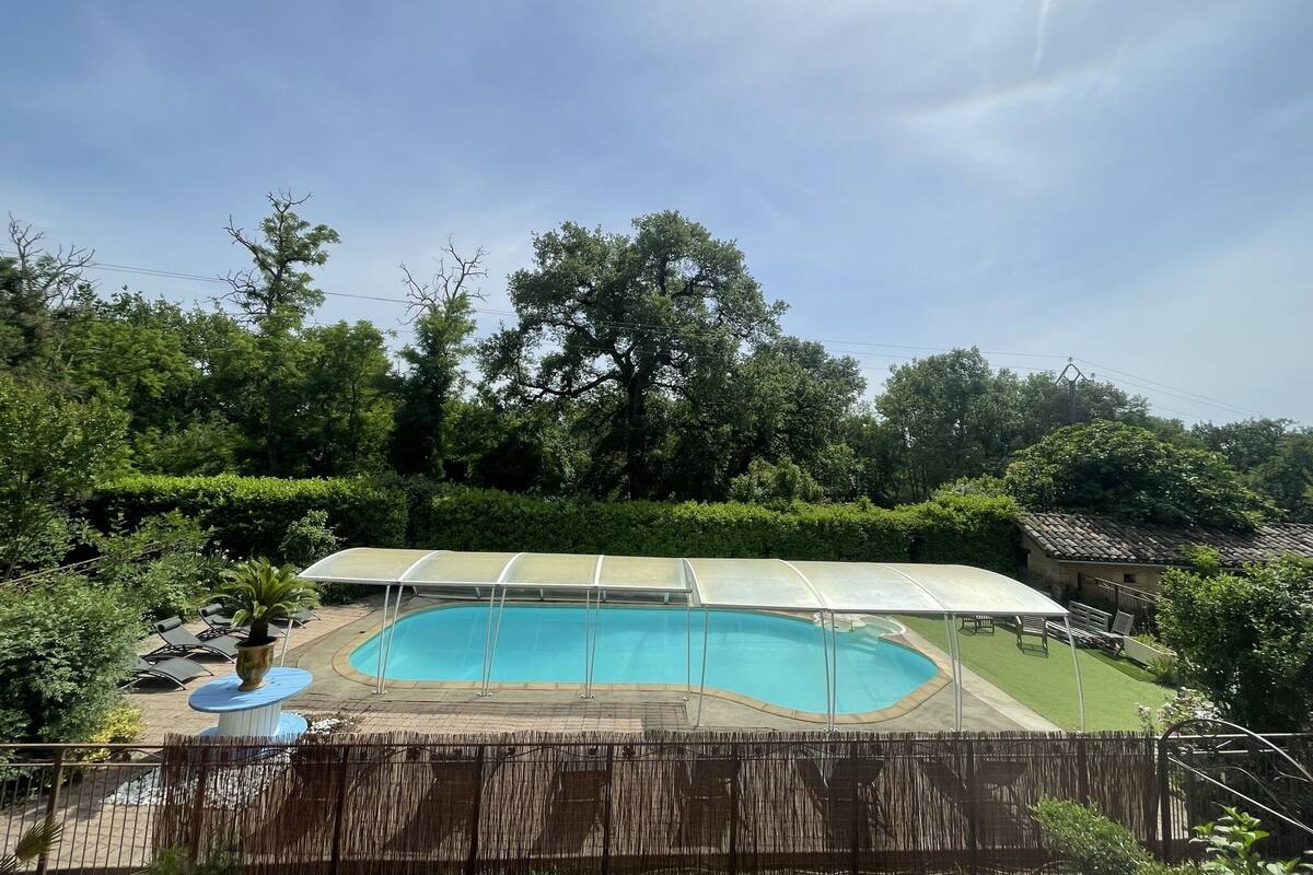 A swimming pool with a covered area, surrounded by lush greenery and trees.