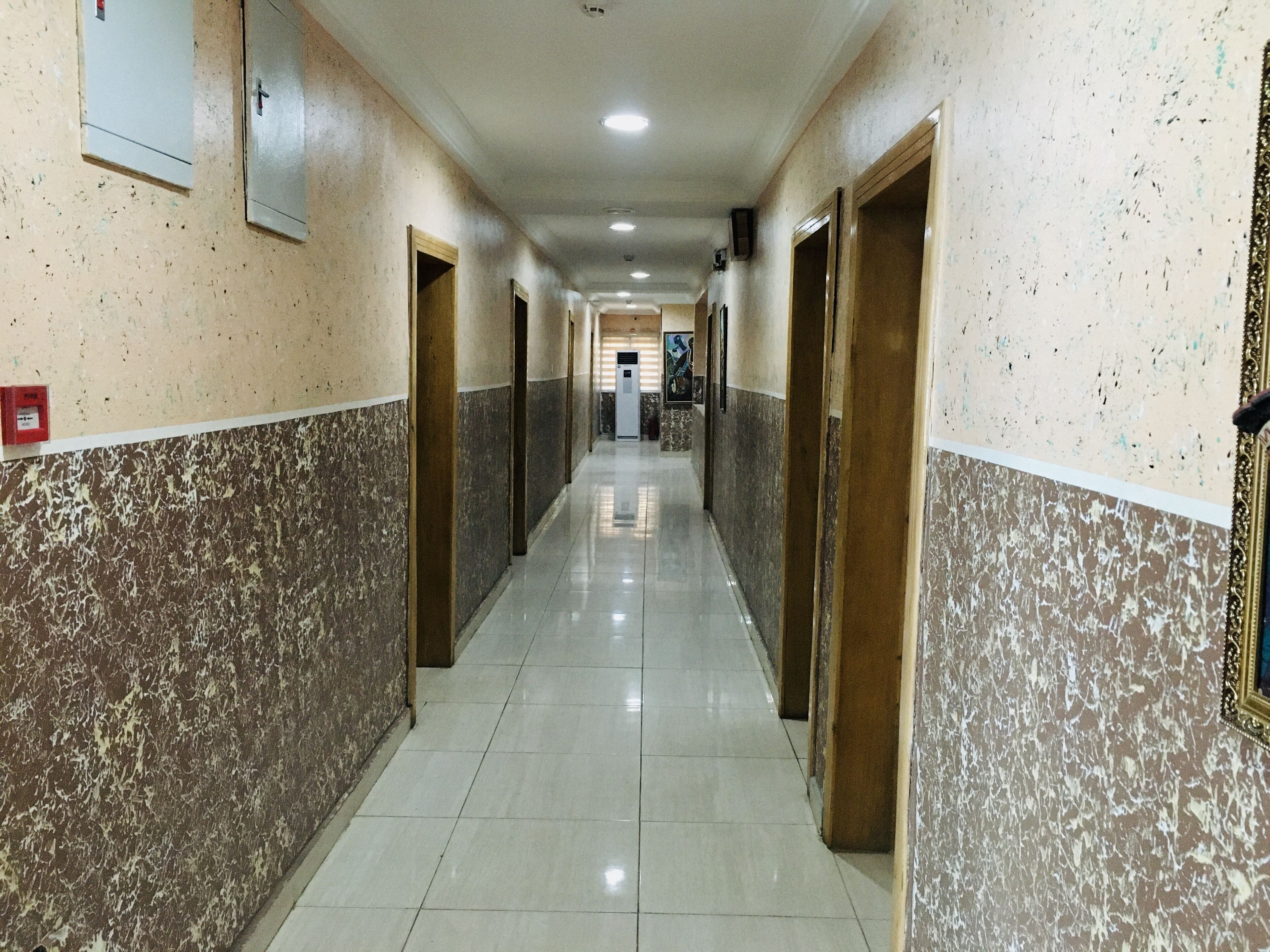 A hallway with marble walls and doors, leading to a reception area with a counter and framed pictures.