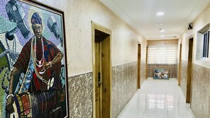 Een gang met een gekaderd kunstwerk links, deuren die naar andere kamers leiden, en een betegelde vloer.