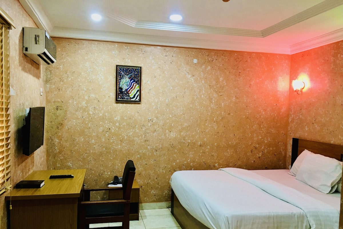 A hotel room with a bed, desk, chair, and a wall-mounted TV.