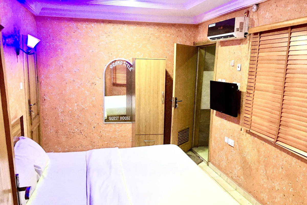 A hotel room with a bed, a mirror, a door, and a television.