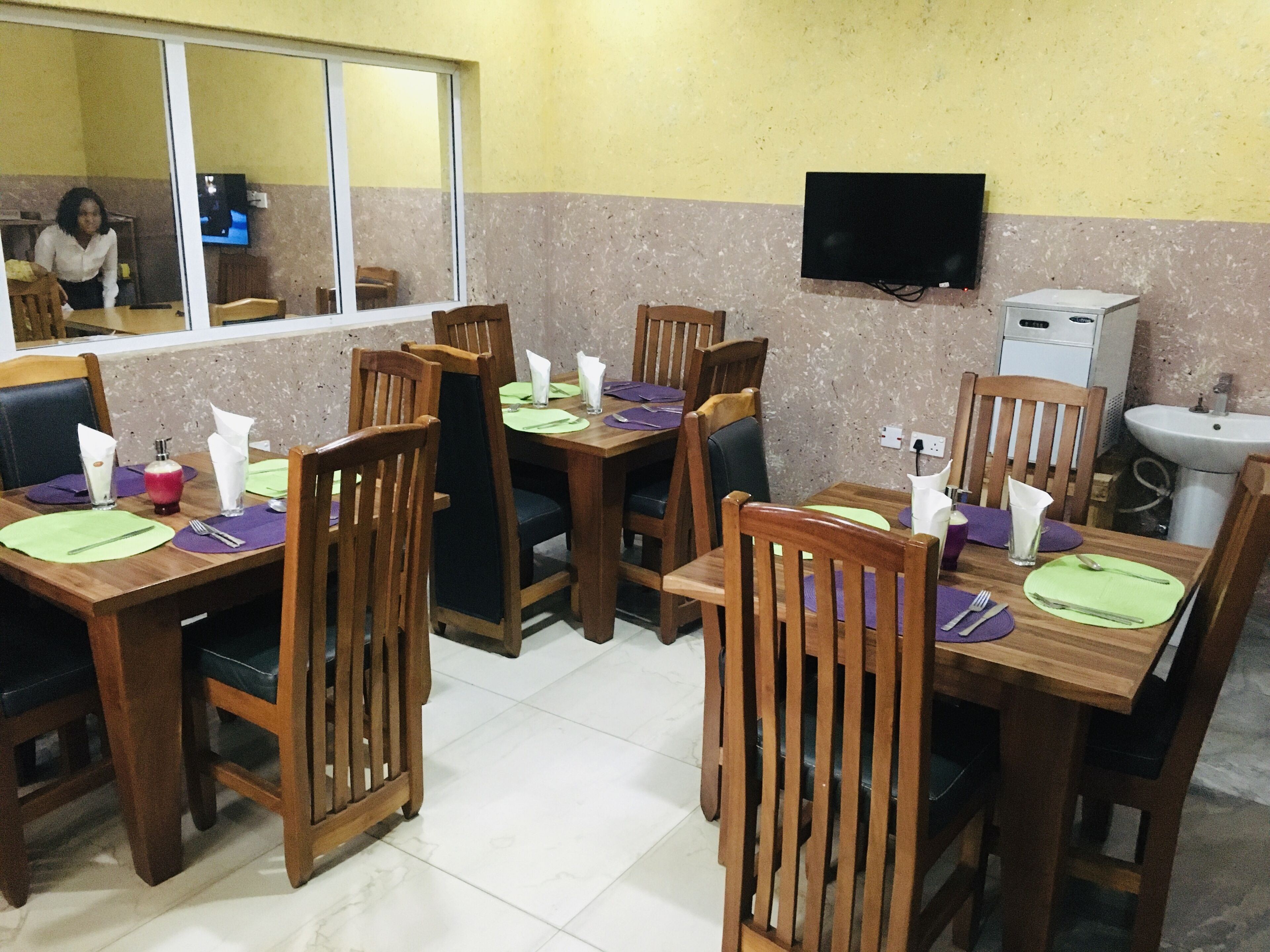 A restaurant with wooden tables and chairs, a TV mounted on the wall, and a sink in the corner.