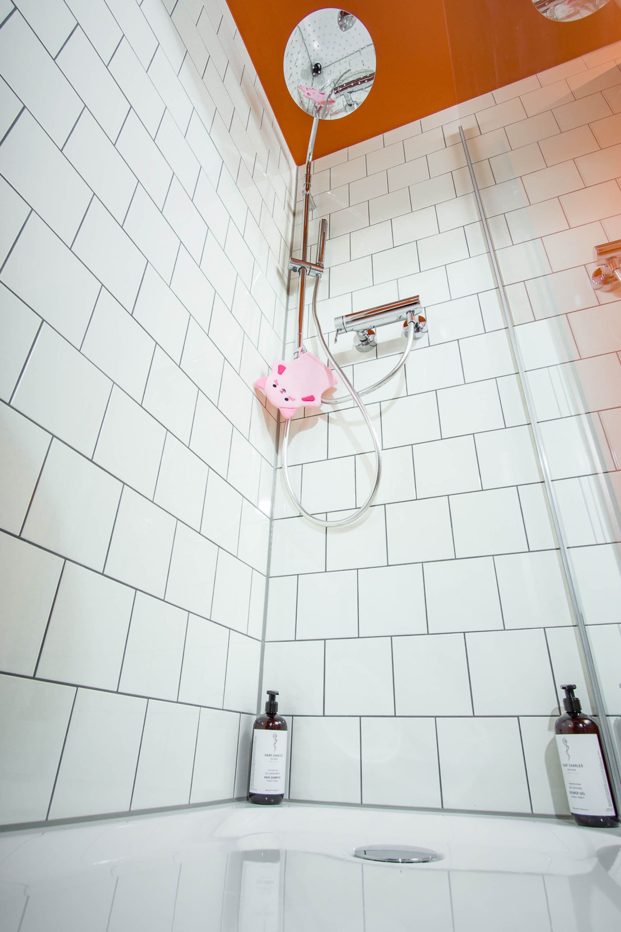 A bathroom with white tiled walls, a white bathtub, and a shower with a pink faucet.