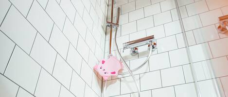 A bathroom with white tiled walls, a white bathtub, and a shower with a pink faucet.