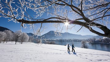 Schneebedeckte Landschaft mit einem See, Bergen und einer wandernden Person.