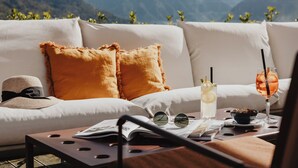Un canapé avec des coussins, une table avec un saladier, des verres et un livre, et une vue sur les montagnes.