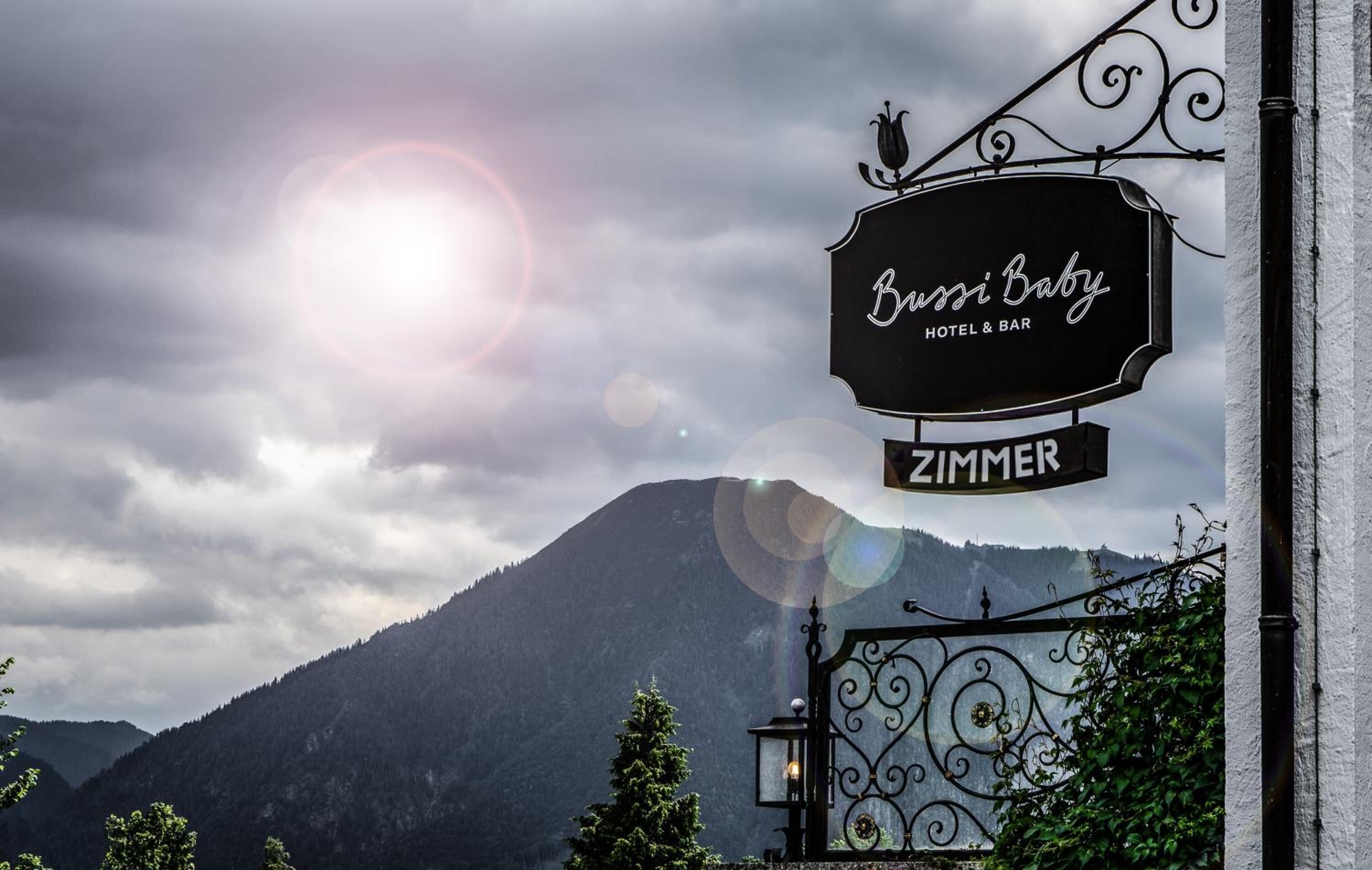 Ein Schild für 'Bussi Baby Hotel & Bar' mit Blick auf einen Berg im Hintergrund.