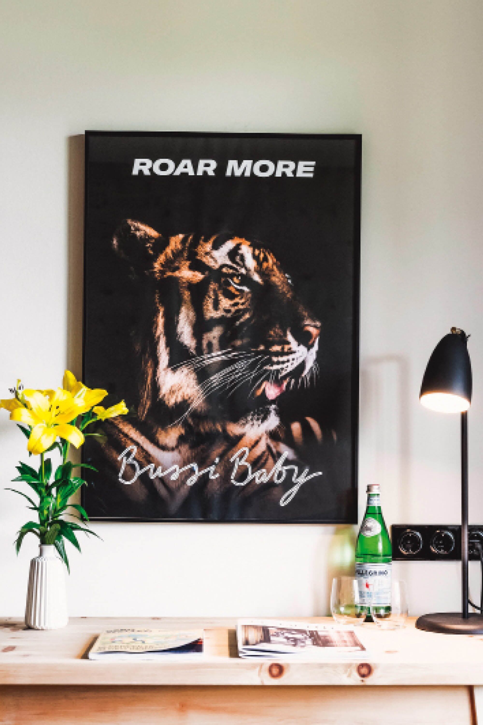 A framed poster of a tiger with the text "ROAR MORE" and "Busi Baby" on a wall.