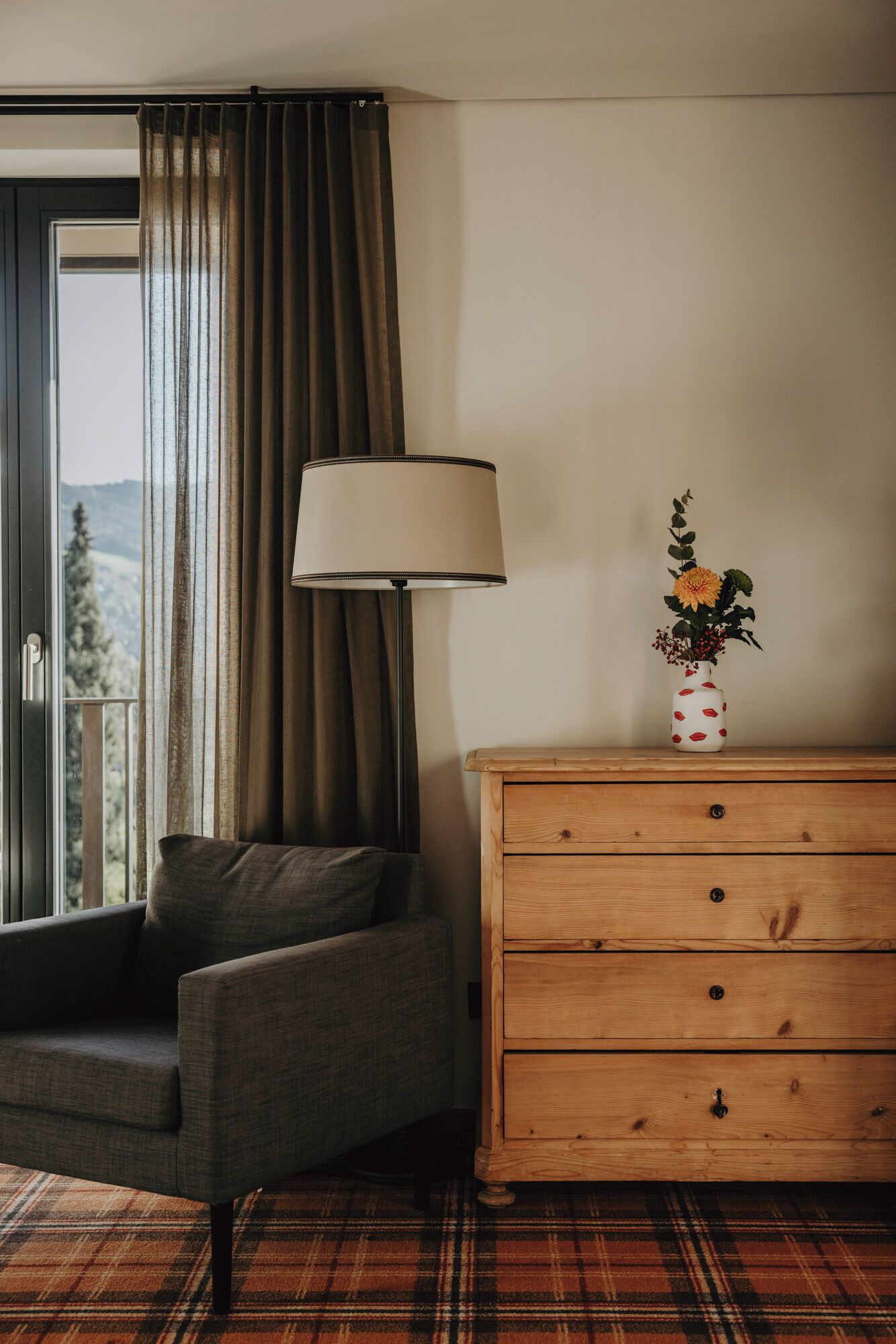Ein Zimmer mit einer Couch, einem Holzkasten, einer Lampe und einer Vase mit Blumen.