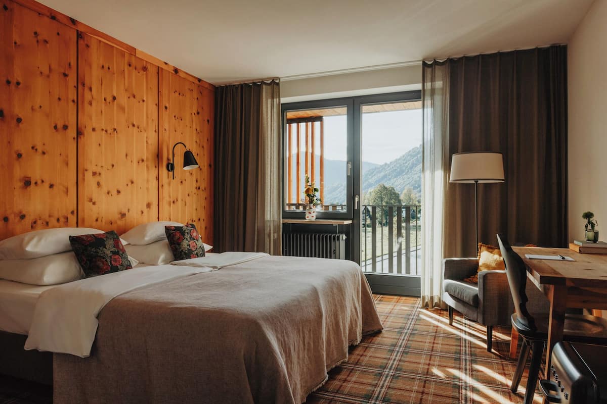 Une chambre d’hôtel avec un lit, un bureau, une chaise, une vue sur les montagnes et un mur en bois.