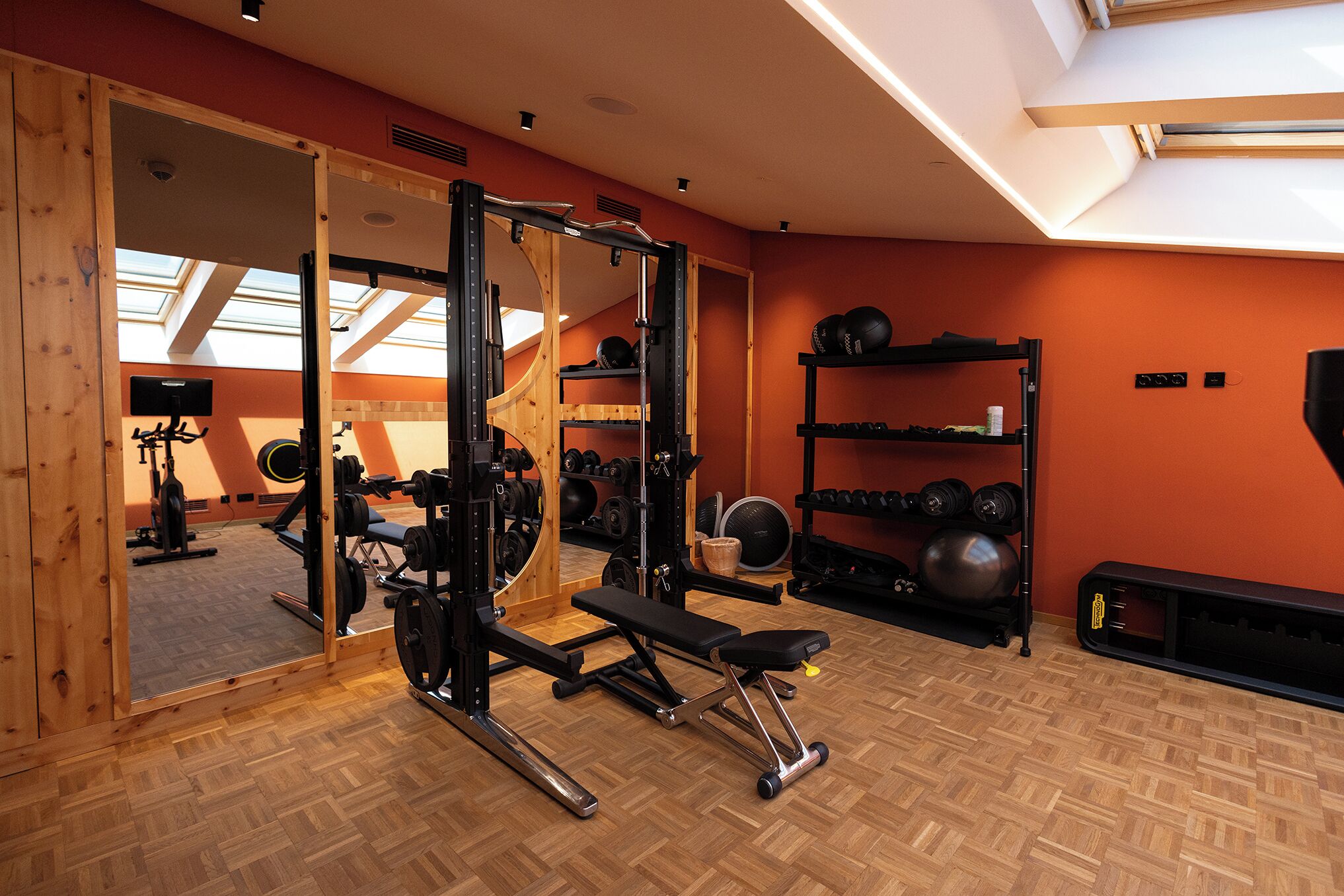 Ein Fitnessraum mit Holzboden, Krafttrainingsgeräten und einer Spiegelwand.