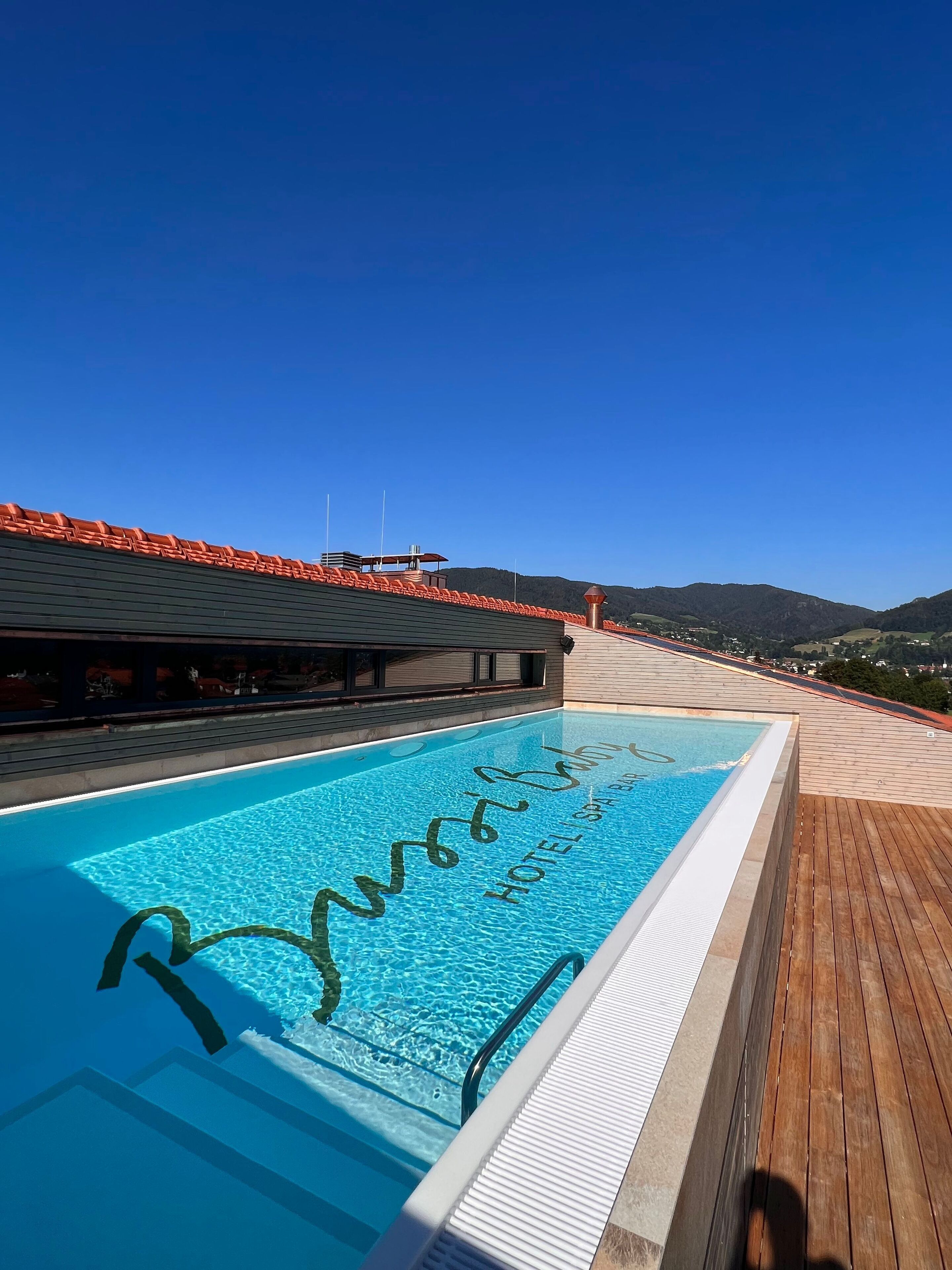 A swimming pool with a wooden deck and a clear blue sky.