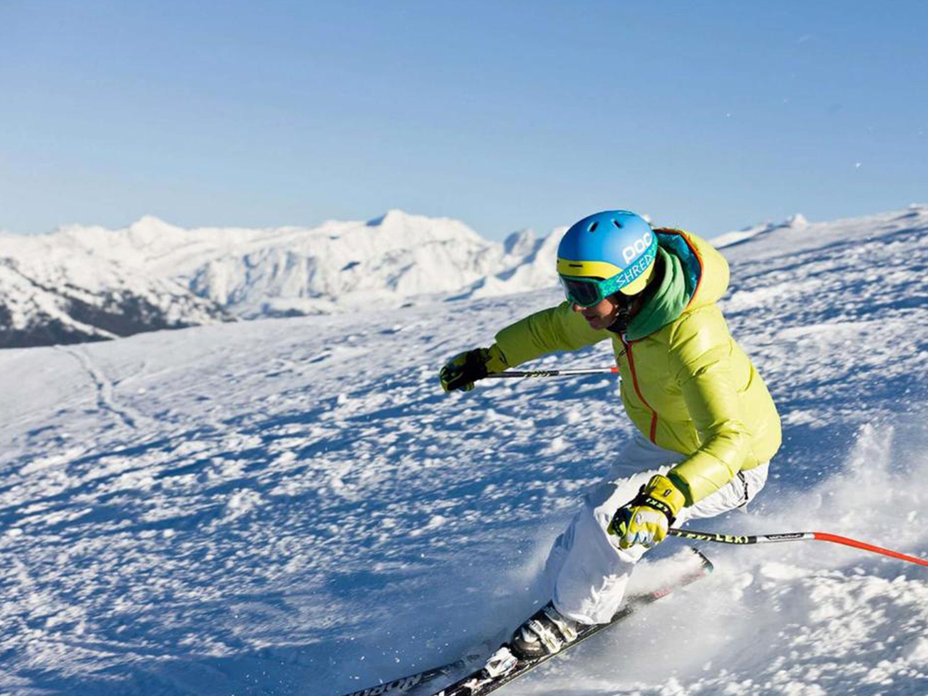 Ein Skifahrer mit gelber Jacke und blauer Helm fährt einen schneebedeckten Hang hinab.