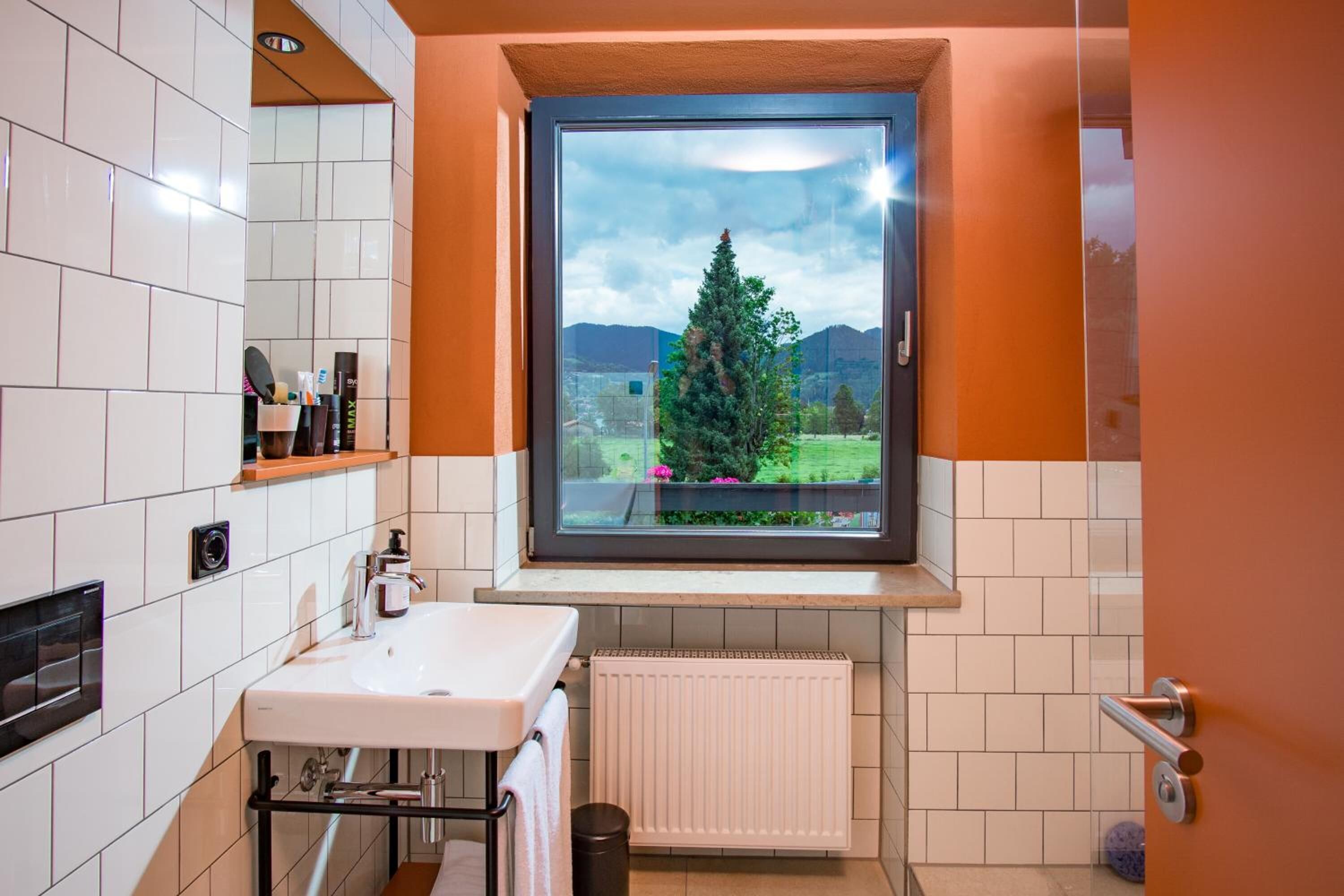 Un baño con vistas al exterior: un árbol y montañas, un lavamanos blanco y un perchero para toallas.