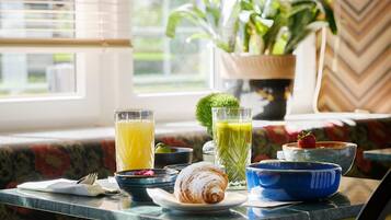 Una mesa de desayuno con un croissant, un vaso de jugo de naranja, un vaso de jugo verde y un tazón de fresas.