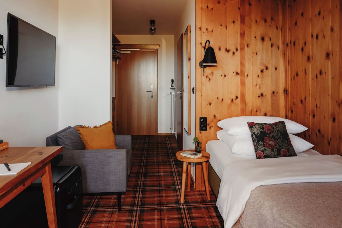 Une chambre d’hôtel avec un lit, un canapé, une petite table, une télévision et un mur en bois.