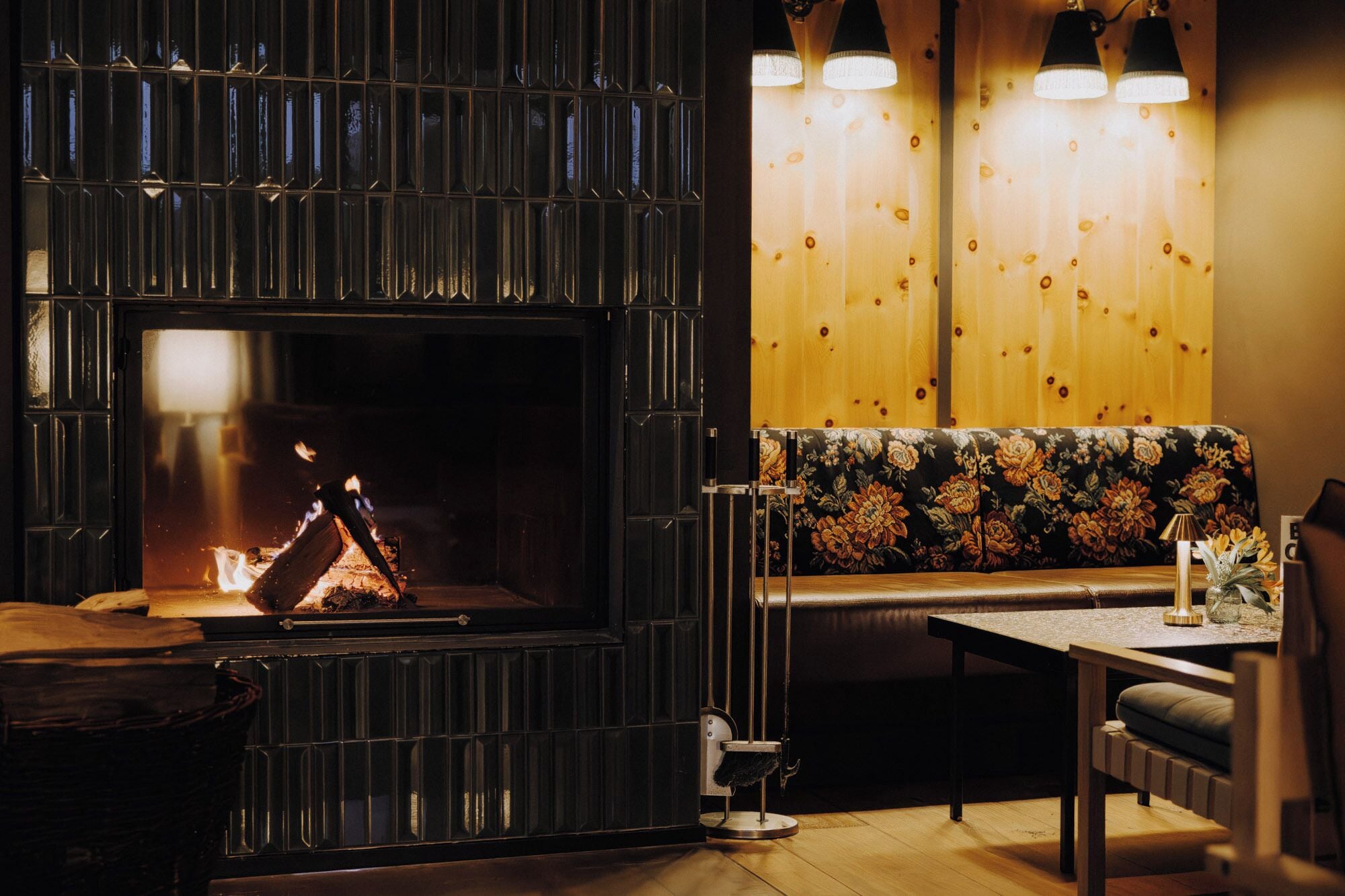 Una habitación acogedora con chimenea, un banco, una mesa y dos lámparas colgantes.