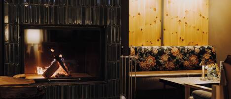 Una habitación acogedora con chimenea, un banco, una mesa y dos lámparas colgantes.