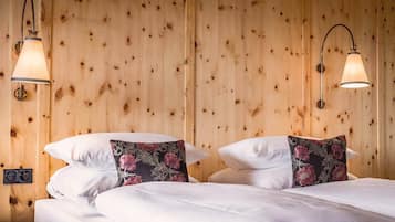 A wooden-paneled room with two beds, each with white bedding and floral-patterned pillows. There are two wall-mounted lamps with a classic design.