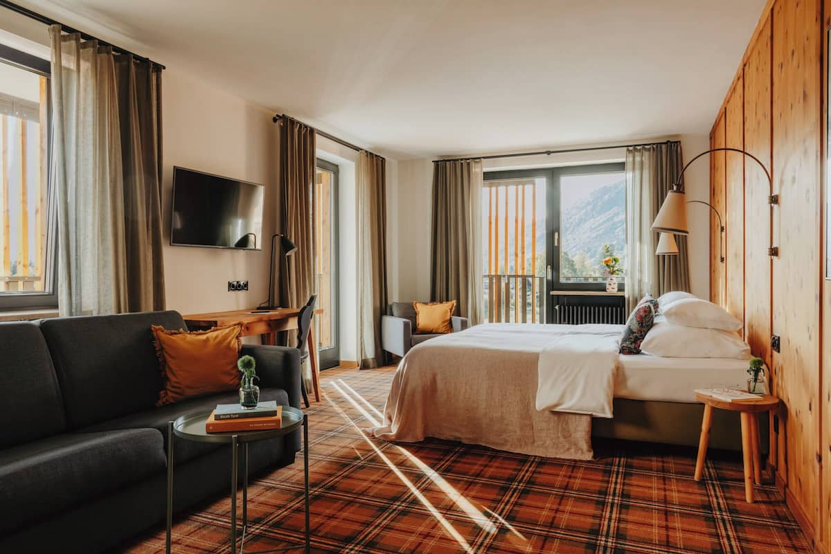 Une chambre d’hôtel avec un lit, un canapé, une télévision, un bureau et une vue sur les montagnes.