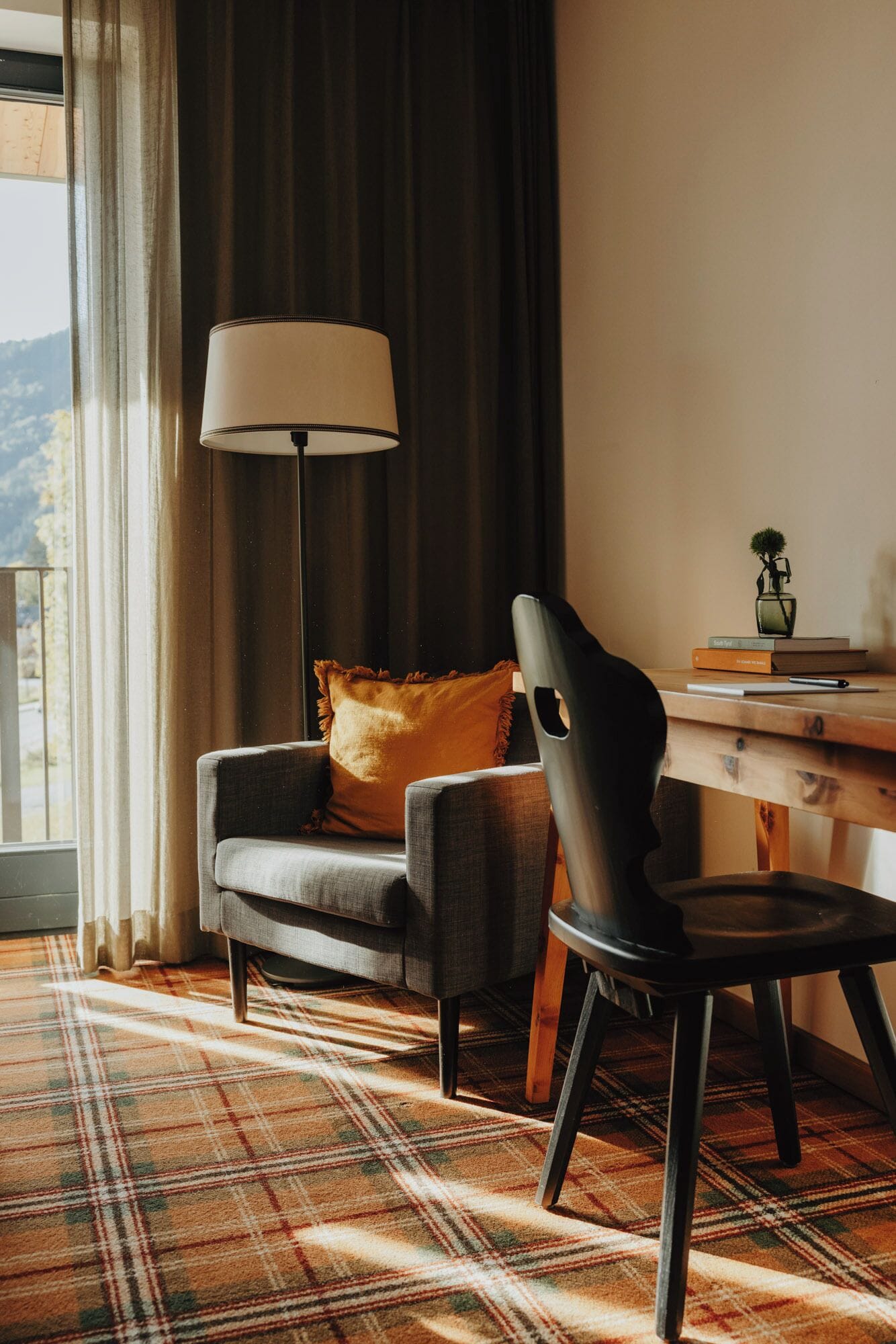 Una habitación acogedora con alfombra escocesa, un sofá con un cojín, un escritorio con lámpara y vistas al exterior.