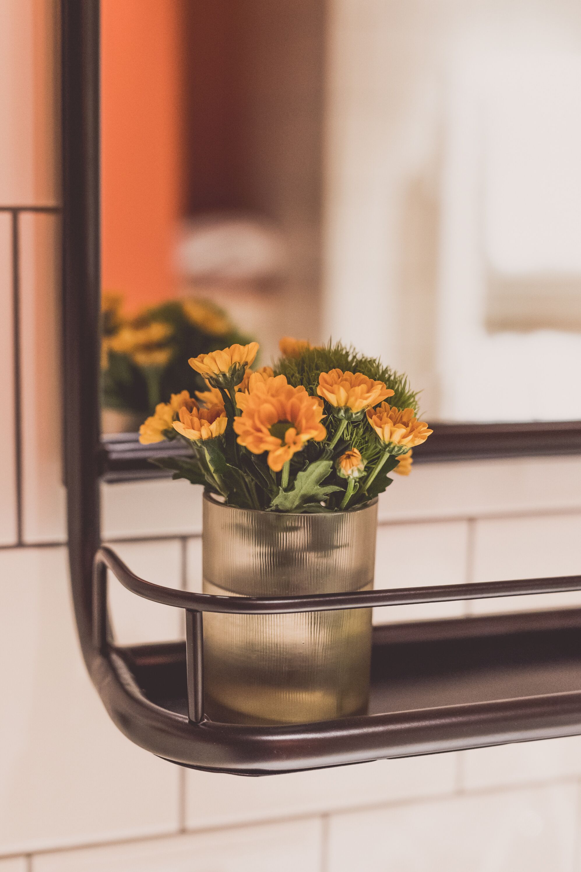 A bathroom with a mirror reflecting a potted plant with yellow flowers.