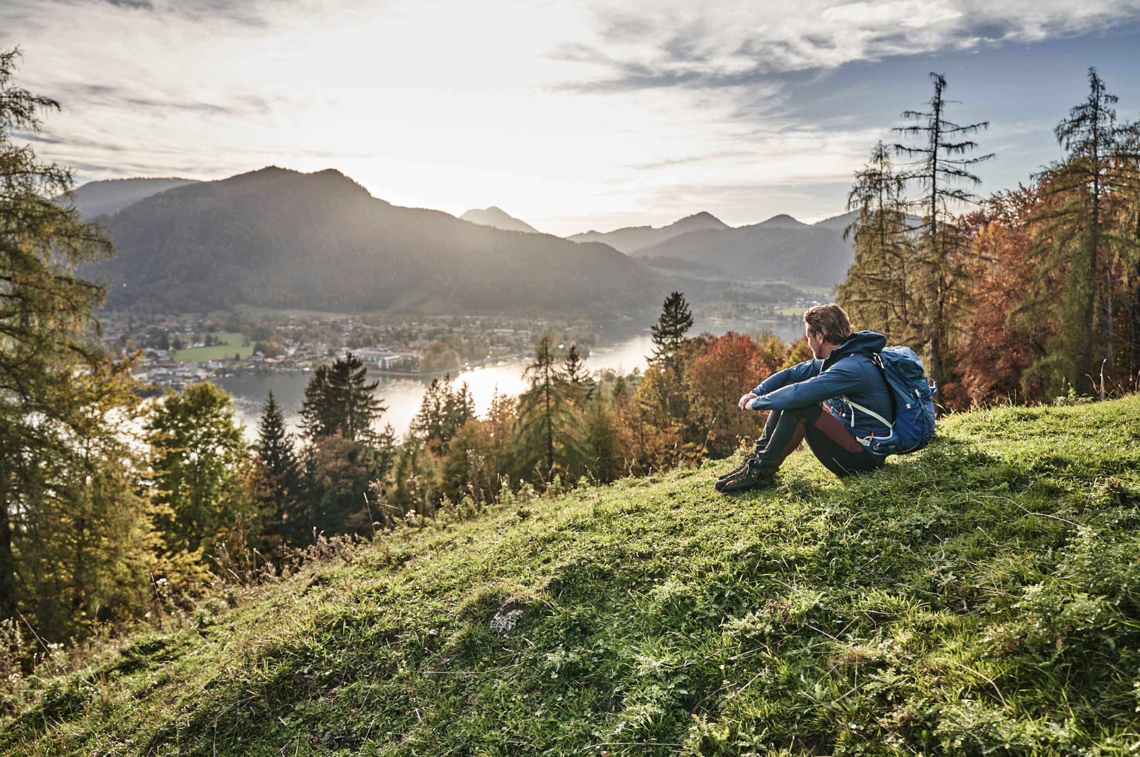A person sitting on a grassy hill overlooking a lake and mountains.