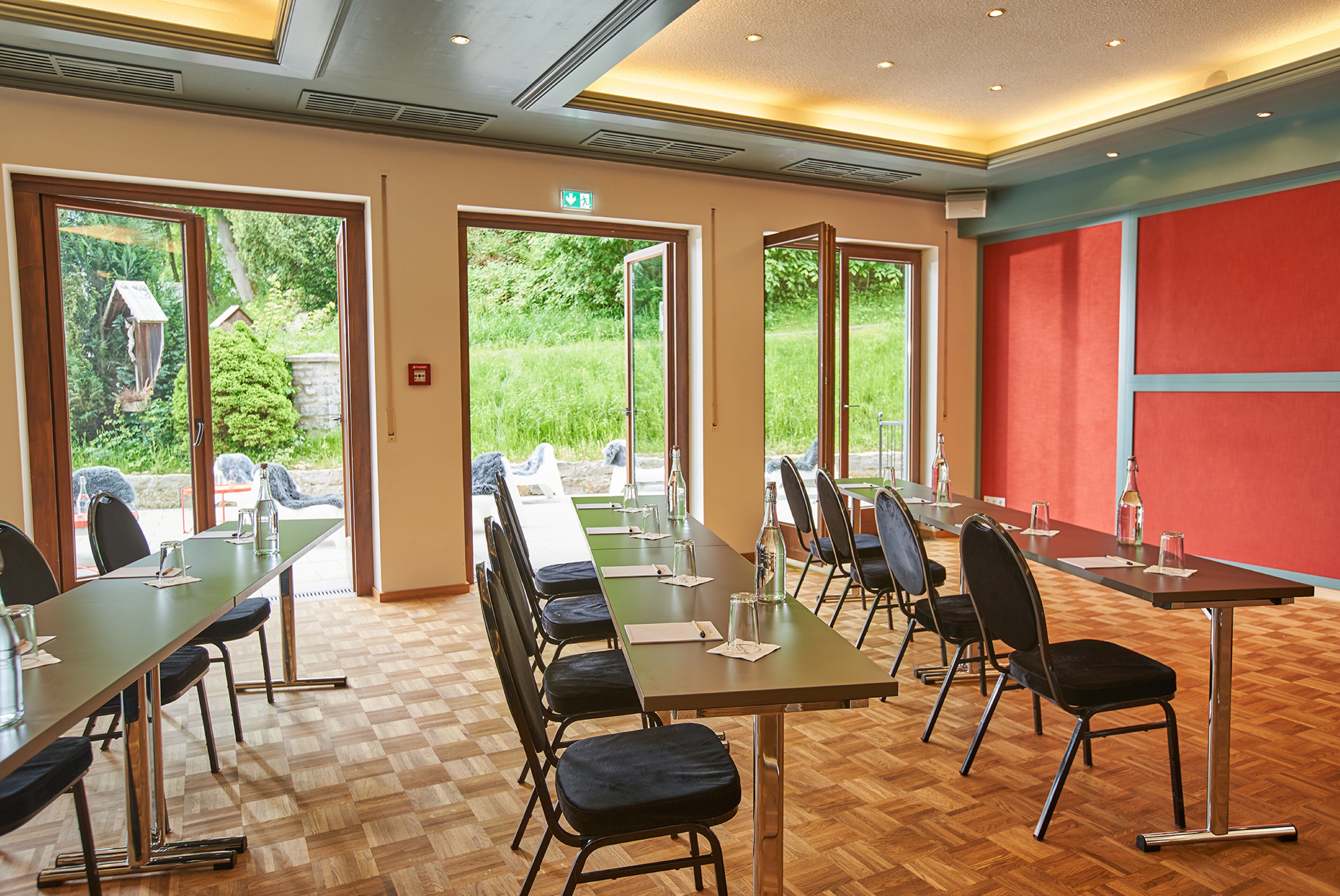 A conference room with a long table, chairs, and a view of greenery outside.