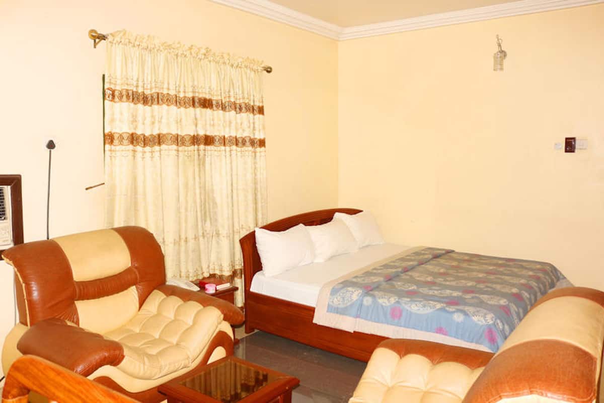 A bedroom with a bed, two armchairs, a nightstand, and a lamp.