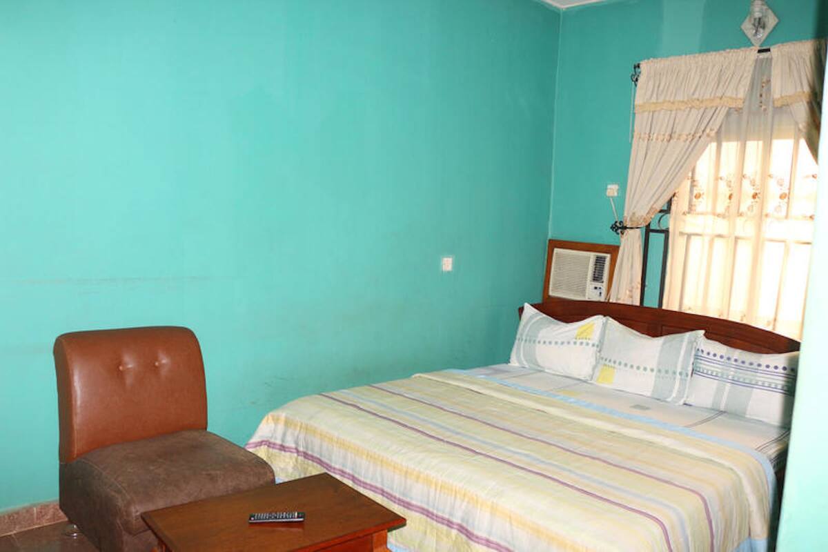 A bedroom with a single bed, a wooden headboard, a brown leather chair, and a small wooden table.