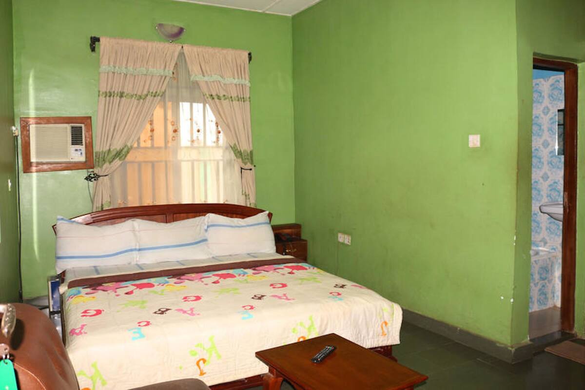 A bedroom with a bed, a bedside table, a window with curtains, and a door with a patterned design.